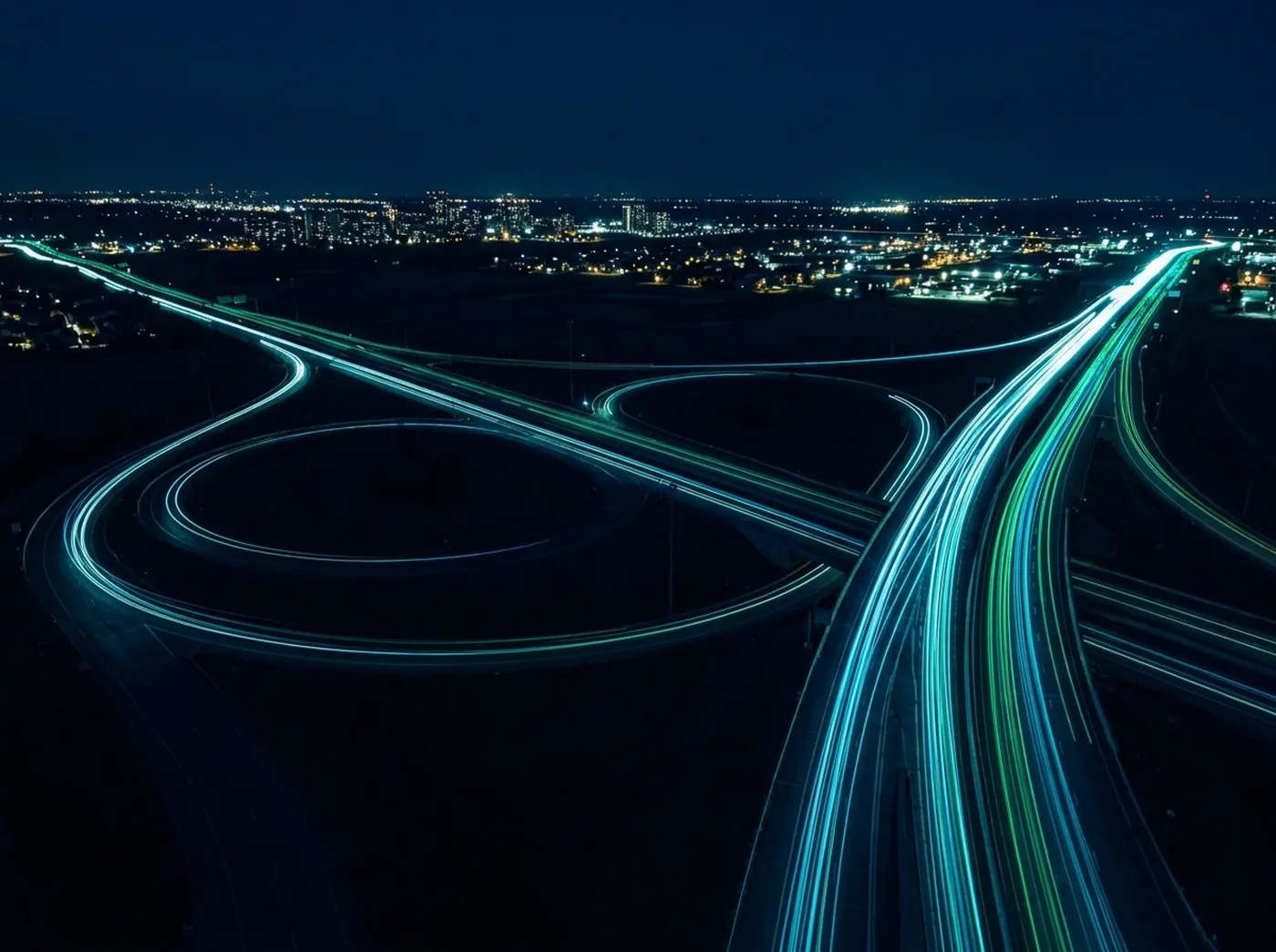 Night highway interchange with streaming light trails between cities